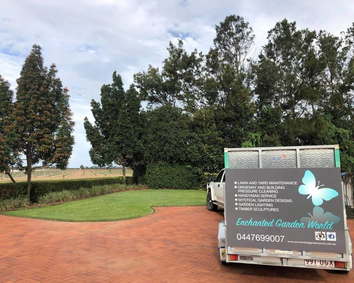 The signwritten Enchanted Garden World ute and trailer parked on a brick driveway beside a mown lawn