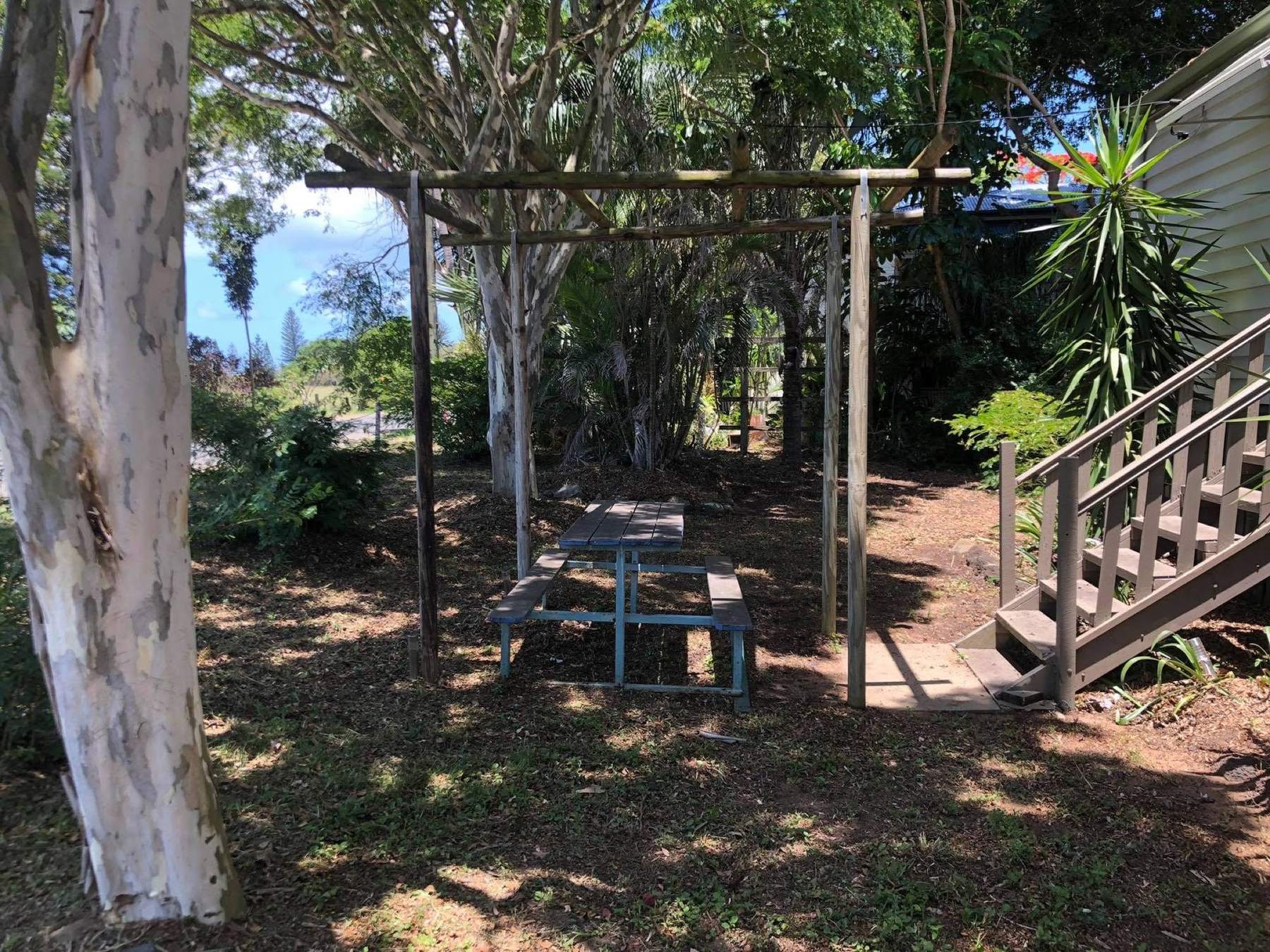 A timber pergola and picnic table under paperbark trees in a shaded yard