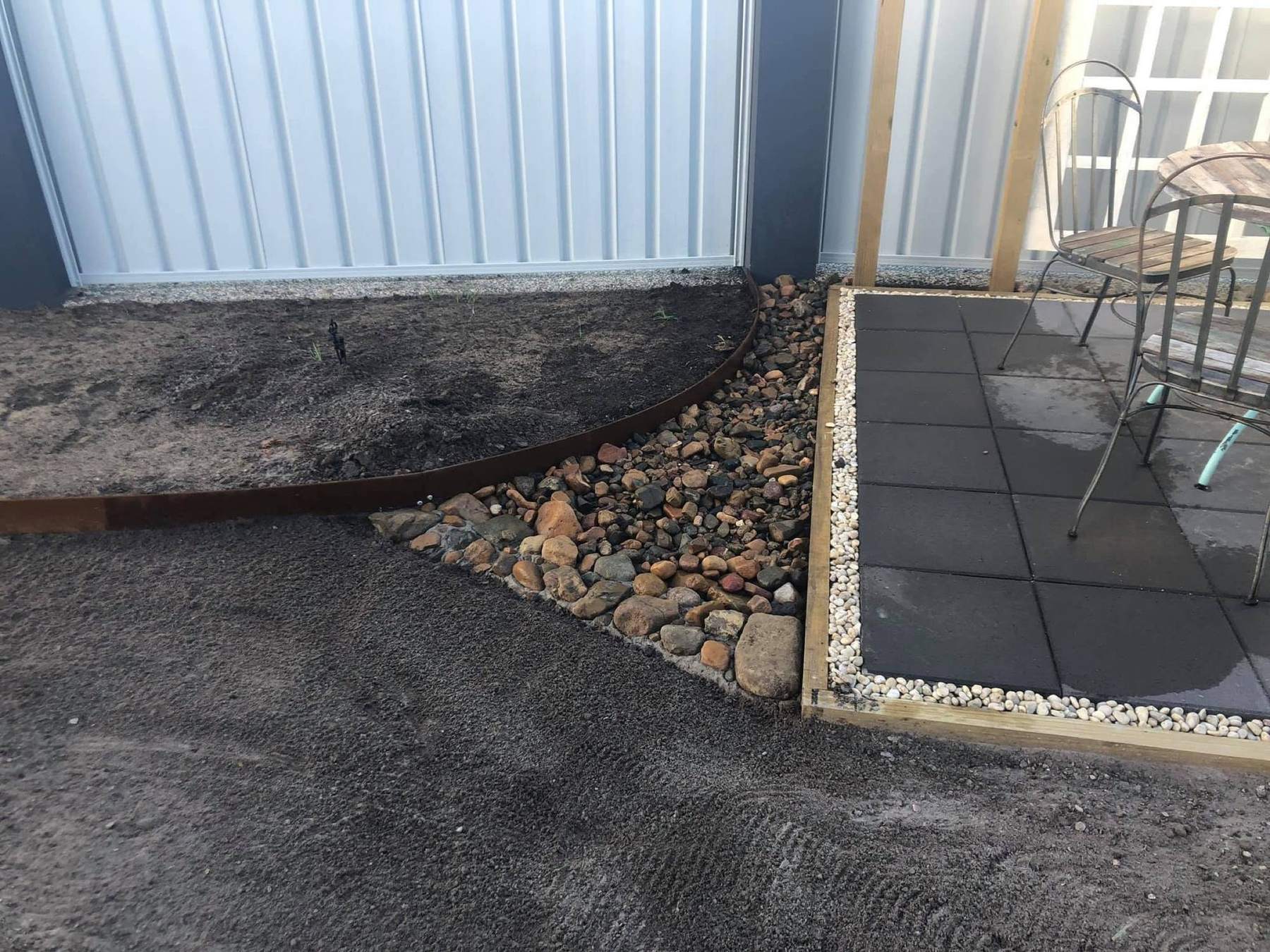A curved garden bed of river pebbles beside a tiled patio