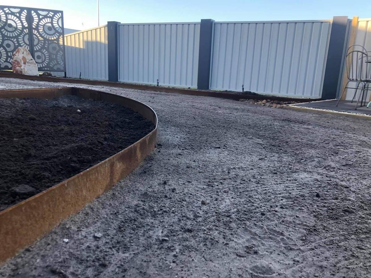 A steel garden edge curving through fresh mulch beside a fence