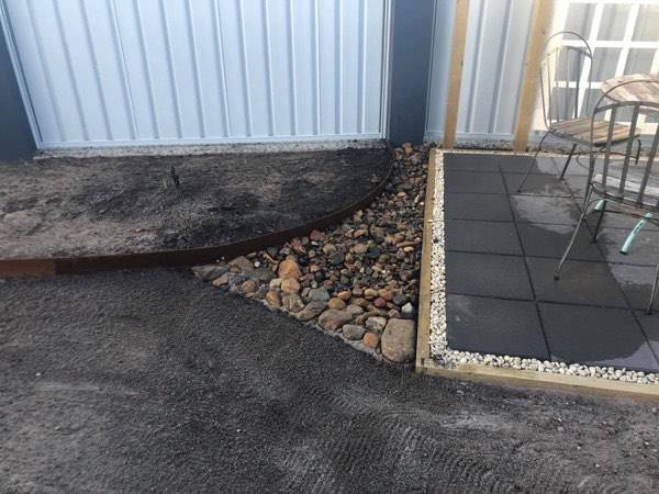 A curved garden bed of river pebbles beside a tiled patio