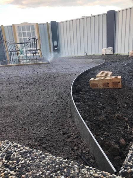 Curved steel edging with a brick sitting on freshly turned soil